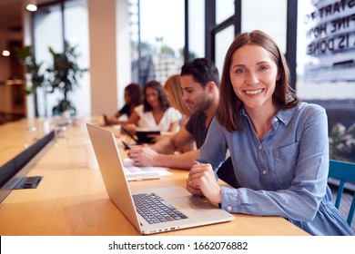 Portrait Of Businesswoman Working At Desk In Shared Open Plan Office Workspace