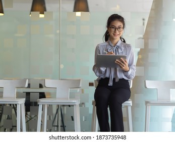 Portrait of businesswoman working with digital tablet while sitting on bar chair in cafeteria