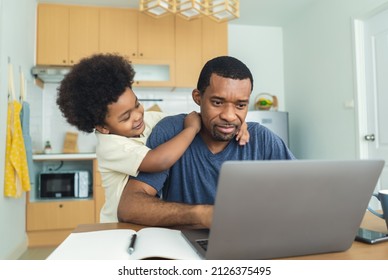 Portrait Of Busy African American Father Working From Home Office Using Laptop Computer Sit At Kitchen Table With Cute Little Son Playing Nearly To Disturb. Exhausted Parent With Hyperactive Child.