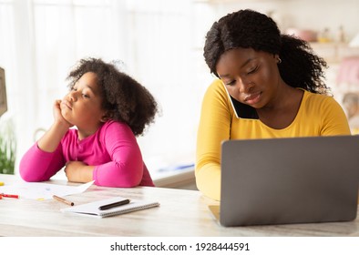 Portrait Of Busy Black Mom Working In Kitchen Next To Her Bored Little Daughter, Cute Female Child Feeling Lonely While Mother Using Laptop And Talking On Cellphone, Managing Remote Business