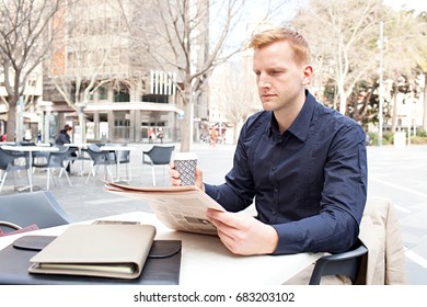 Portrait Of Busy Businessman Reading Financial Newspaper Drinking Cup Of Coffee In Coffee Shop In Classic City, Outdoors. Smart Professional Successful Man With Folders Paperwork Holding Paper. 