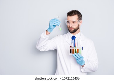 Portrait of busy concentrated scientist with stubble in white lab coat, gloves analysing, looking at  test tubes with multi-colored liquid in his arm, isolated on grey background - Powered by Shutterstock