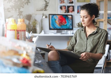 Portrait Of Busy Confident Young Brunette Woman Designer In Ripped Jeans Working On New Art Project, Making Drawings Or Sketches On Tablet. Beautiful Female Artist Absorbed With Her Creative Work