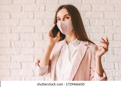 Portrait busy young girl entrepreneur in pink medical face mask and suit talk cell phone. Happy beautiful business woman in pink protective face mask have business communication on mobile phone