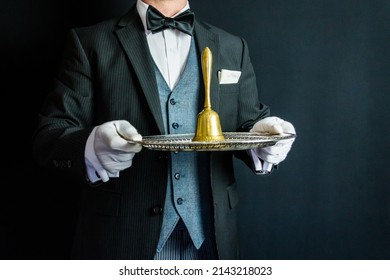 Portrait of Butler in Dark Formal Suit and White Gloves Holding Gold Bell on Silver Tray. Concept of Service Industry and Professional Hospitality.