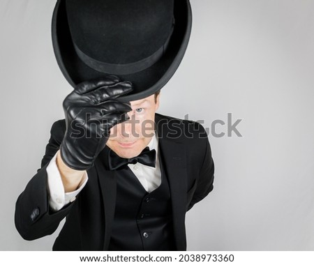 Portrait of Butler in Dark Suit Politely Bowing and Doffing Bowler Hat on White Background. Concept of Service Industry and Professional Hospitality. Classic English Gentleman.