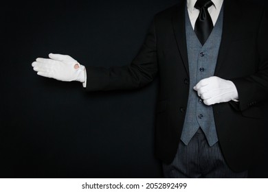 Portrait of Butler in Dark Suit and White Gloves Standing with Welcoming Gesture on Black Background. Copy Space for Service Industry and Professional Courtesy.