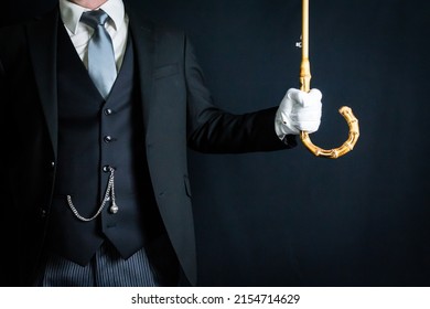 Portrait Of Butler Or Doorman In Dark Suit Offering Umbrella. Copy Space For Service Industry And Professional Hospitality.