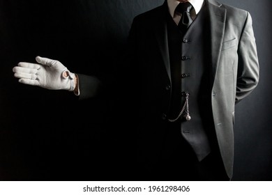 Portrait of Butler or Servant in Dark Suit and White Gloves With Welcoming Gesture on Black Background. Concept of Service Industry and Professional Hospitality. 