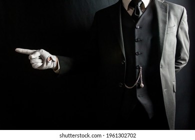 Portrait of Butler or Servant in Dark Suit and White Gloves Pointing the Way on Black Background. Concept of Service Industry and Professional Hospitality.