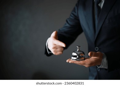Portrait of Butler or Waiter in Black Suit and White Gloves Holding Gold Bell. Ring for Service Concept. 