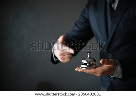 Portrait of Butler or Waiter in Black Suit and White Gloves Holding Gold Bell. Ring for Service Concept. 