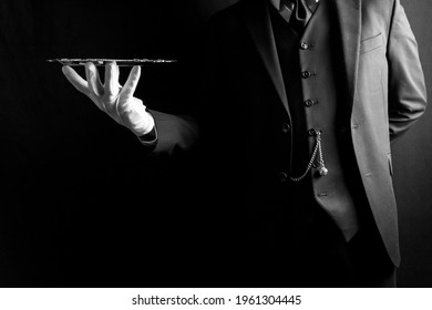 Portrait of Butler or Waiter in Dark Suit and White Gloves Expertly Holding Silver Tray on Black Background. Concept of Service Industry and Professional Hospitality. 