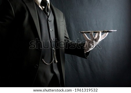 Portrait of Butler or Waiter in Dark Suit and White Gloves Holding Silver Tray on Black Background. Concept of Service Industry and Professional Hospitality.
