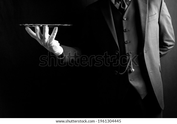Portrait of Butler or Waiter\
in Dark Suit and White Gloves Expertly Holding Silver Tray on Black\
Background. Concept of Service Industry and Professional\
Hospitality. 