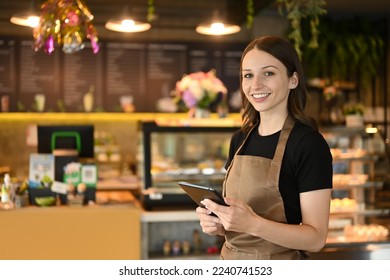 Portrait of cafe owner smiling cheerfully using a digital tablet in front of the counter in modern coffee chop - Shutterstock ID 2240741523