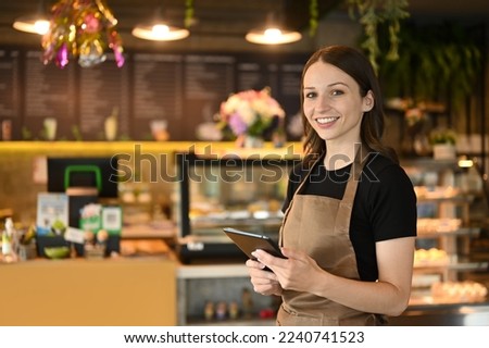 Portrait of cafe owner smiling cheerfully using a digital tablet in front of the counter in modern coffee chop