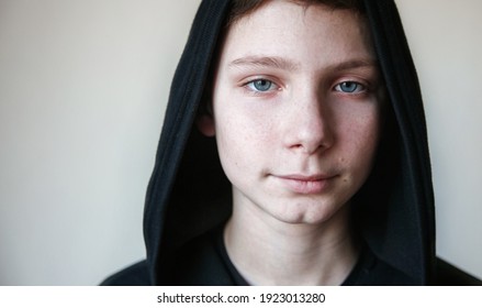 Portrait of a calm blue-eyed teenage boy in a black hood. High quality photo