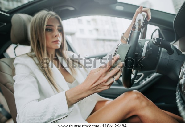 Portrait of calm female typing in mobile while\
situating on chair of modern car. Orderly girl using appliance in\
vehicle concept