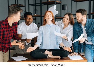 Portrait of calm young business woman meditate at business meeting avoiding pressure annoying angry colleagues. Meditative businesswoman yoga exercises for stress relief. Coworkers shaking documents. - Powered by Shutterstock