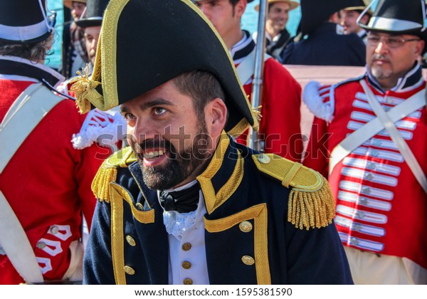 Portrait of a captain of the 1800s Royal Navy.\
Reenactor wearing a british uniform, blue frock coat and bicorn\
hat. People behind with the royal marines uniform. Málaga, Spain -\
October 26, 2014.