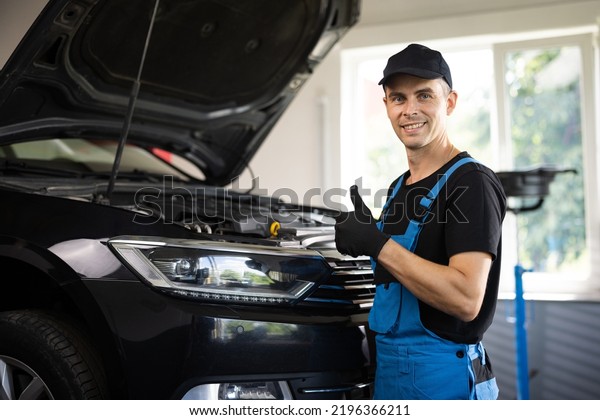 Portrait of car mechanic in a car workshop shows\
thumbs up, in the background of service. Positive auto service\
worker smiling to camera and showing thumb up gesture, approving\
car repair workshop