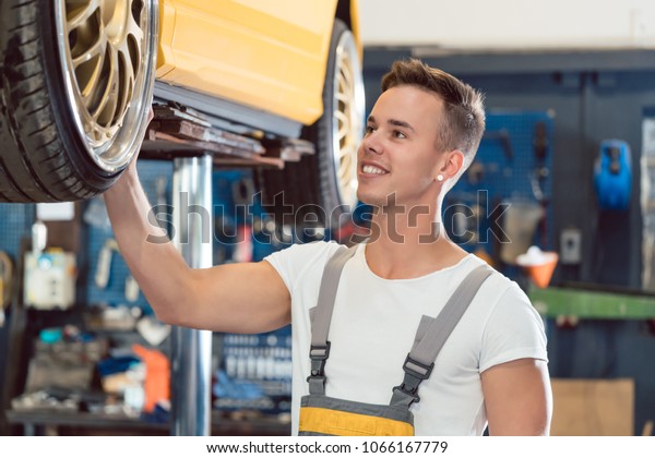 Portrait of a car tuning specialist smiling,\
while checking the wheels of a tuned lifted car with cool modified\
rims in a trendy automobile repair\
shop