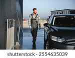 Portrait of a car wash worker. A handsome worker in a uniform stands near a washed car.