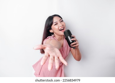 Portrait of carefree Asian woman, having fun karaoke, singing in microphone while standing over white background - Powered by Shutterstock