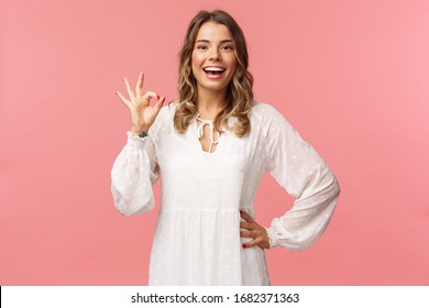 Portrait of carefree good-looking blond girl, wear white dress, guarantee you will like this special spring offer, show okay sign, agree or accept, smiling and nod in approval, pink background - Shutterstock ID 1682371363
