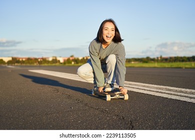 Portrait of carefree, happy asian girl skating, riding skateboard and laughing, enjoying sunny day. - Powered by Shutterstock