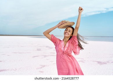 Portrait of carefree pleased woman in pink dress enjoying travel on salt flats beach with blue sky at pink lake.