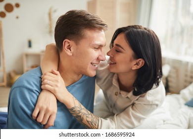Portrait of carefree young couple embracing while sitting on bed and looking at each other with love, copy space