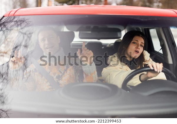 Portrait of carefree young couple\
singing in car while driving to winter vacation\
together