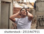 Portrait of a carefree young man with hands up in his hair, while standing in front of a slum area. A proud filipino lbgt male residing in an squatter area. Shantytown background.