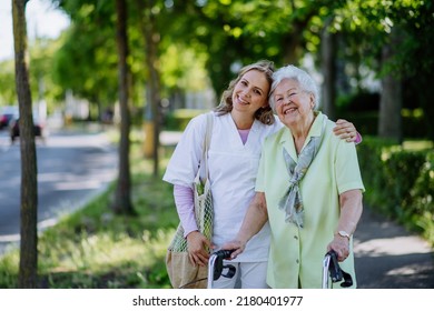 Portrait Of Caregiver With Senior Woman On Walk In Park With Shopping Bag, Looking At Caemra.