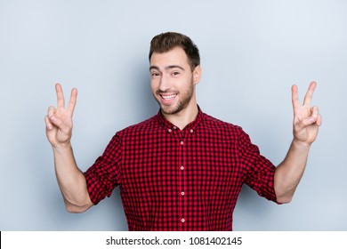 Portrait of careless cheerful relaxed free and easy guy clothed in red checkered shirt demonstrating two fingers, isolated on gray background