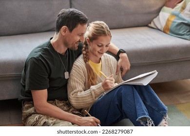 Portrait of caring military father helping daughter doing homework while sitting on floor together - Powered by Shutterstock