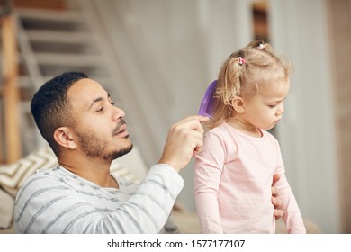 Portrait Of Caring Stay At Home Dad Brushing Hair Of Cute Little Daughter At Home