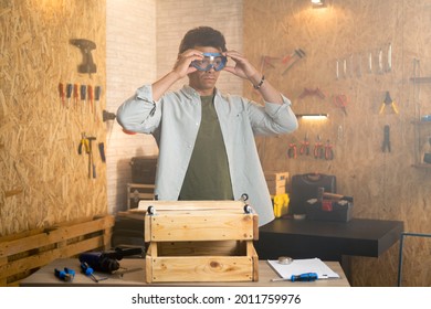 Portrait Of A Carpenter Putting On Safety Goggles Over His Head In His Workshop.