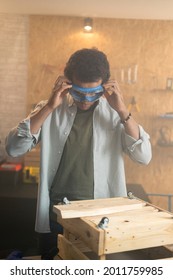 Portrait Of A Carpenter Putting On Safety Goggles Over His Head In His Workshop.