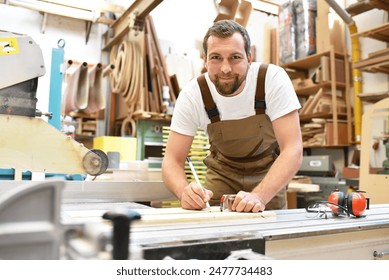 portrait of a carpenter in work clothes and hearing protection in the workshop of a carpenter's shop  - Powered by Shutterstock