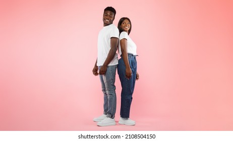 Portrait Of Casual African American Young Couple Standing Back To Back And Looking At Each Other, Guy And Lady Posing Isolated Over Pink Studio Wall, Full Body Length, Panorama Banner, Free Copy Space