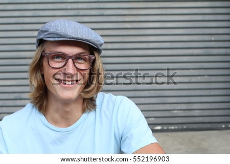 Portrait of casual blonde young man wearing glasses, news paperboy hat and blue crew neck t-shirt smiling and laughing with copy space
