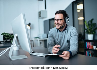 Portrait of a casual smiling businessman using headset when talking to customer.