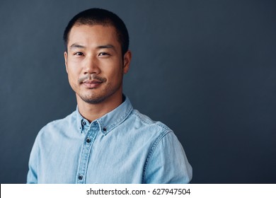 Portrait Of A Casually Dressed Young Asian Designer Smiling Confidently While Standing Against A Gray Wall In An Office