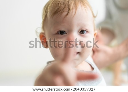 Portrait of Caucasian adorable baby boy kid smile, looking at camera. Cute little young toddler son feel happy while learn to walk on floor in house with parents support. Children development concept.