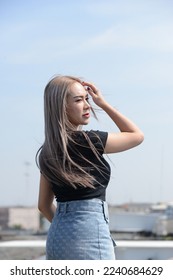 portrait of caucasian beauty girl ashen hair wear black t shirt and jean skirt standing rroftop with small city view - Shutterstock ID 2240684629