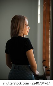 portrait of caucasian beauty girl ashen hair wear black t shirt and jean skirt standing with window light - Shutterstock ID 2240784967