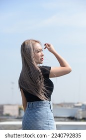 portrait of caucasian beauty girl ashen hair wear black t shirt and jean skirt standing rroftop with small city view - Shutterstock ID 2240792835
